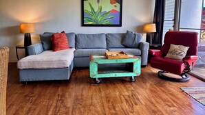 Een woonkamer met een grijze bank, een rode fauteuil, een klein turquoise bijzettafeltje en een schilderij aan de muur.