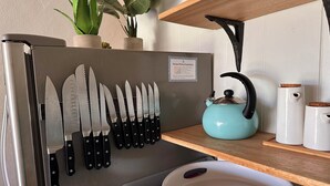 Een keuken met een messenrek, een blauwgroene waterkoker en een witte pan op een plank.