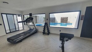 Ein geräumiger Raum mit Laufband, Ergometer und großem Fenster mit Blick auf einen Swimmingpool.