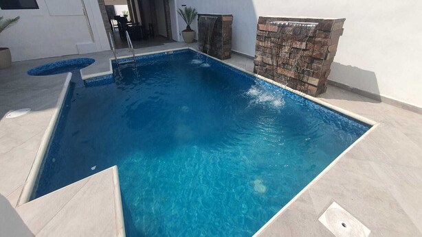 Ein rechteckiger Swimmingpool mit klarem, blauem Wasser, umgeben von einem hell gefliesten Deck.