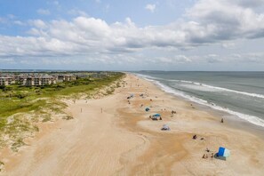 A beach with a row of buildings, some beach umbrellas, and a few people.