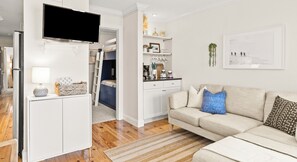 A modern living room with a sofa, a TV, a kitchen area, and a bedroom with a bunk bed.