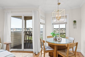 A room with a glass table, wooden chairs, a chandelier, and a view of a balcony with chairs.