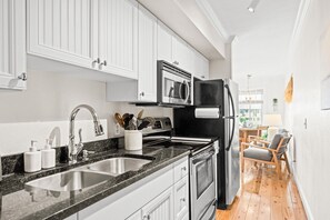 A modern kitchen with stainless steel appliances, white cabinetry, and a wooden dining area.