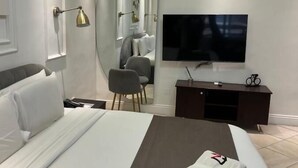 Ein modernes Hotelzimmer mit einem großen Bett, einem Flachbildfernseher, einer dunklen Holzkommode und einem Spiegel an der Wand.