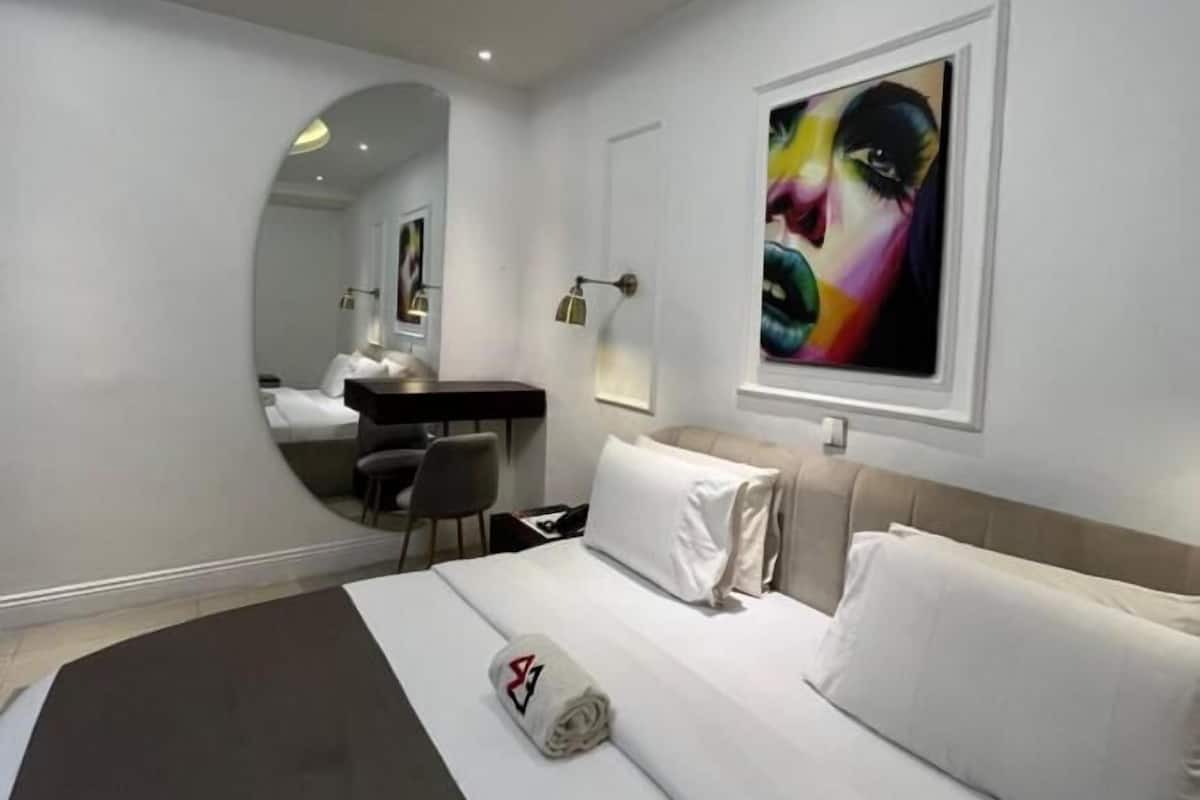 Een moderne hotelkamer met een gebogen plafond, een bed met witte lakens, een bureau met stoel en een groot abstract schilderij aan de muur.