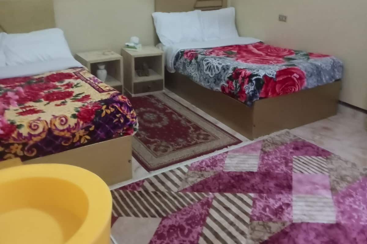 Ein Hotelzimmer mit zwei Betten, einem kleinen Nachttisch, einem gelben Sessel und einem Teppich mit Muster.