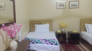 A hotel room with a bed, a nightstand with a vase of flowers, a bedside table with a lamp, and a mirror on the wall. - tut amun guest house (Abu Simbel)