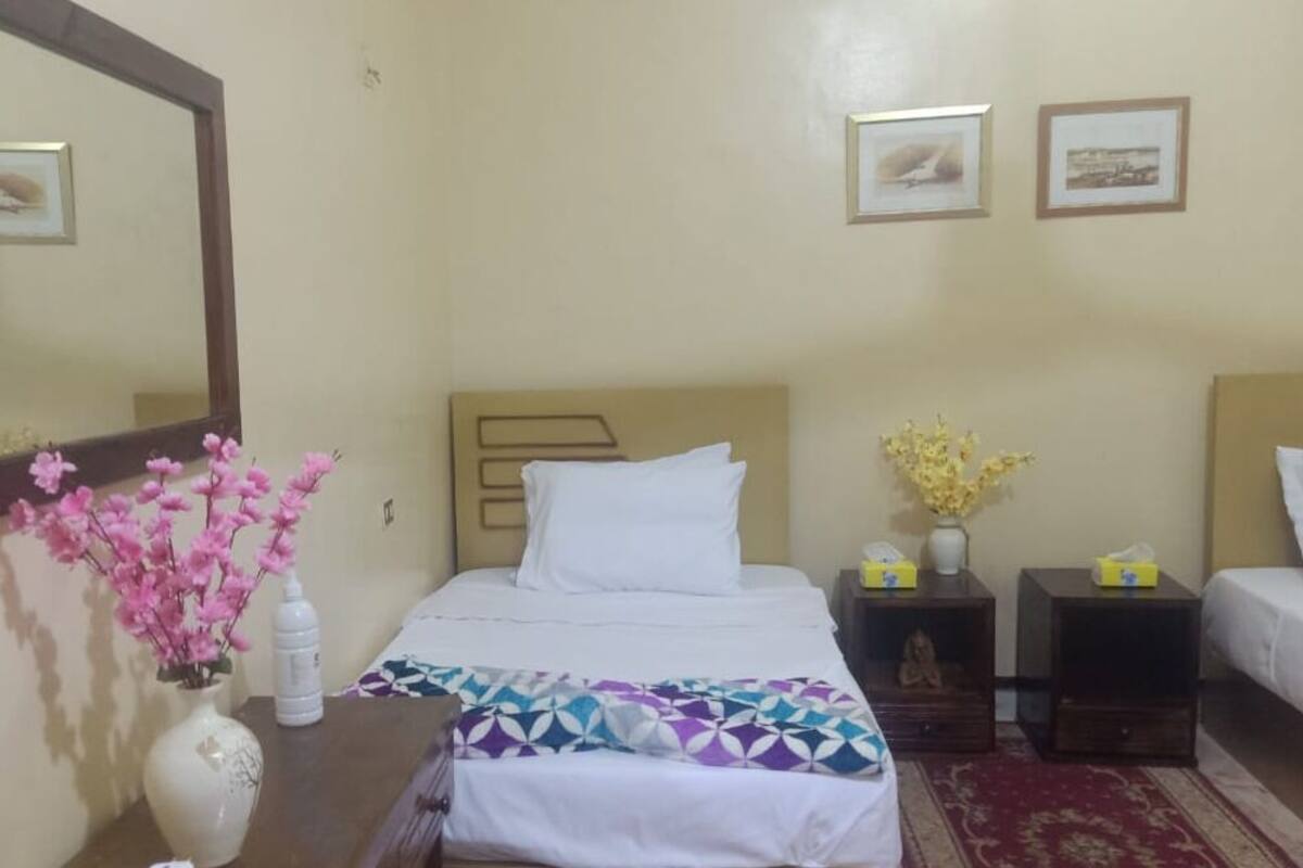 Ein Hotelzimmer mit Bett, Nachttisch mit Blumenvase, Nachttischlampe und Spiegel an der Wand.