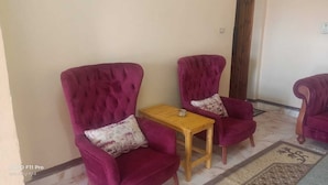 A room with two purple armchairs, a small wooden table, and a patterned rug. - tut amun guest house (Abu Simbel)