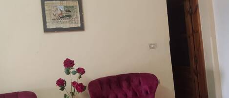 Ein Zimmer mit zwei bequemen roten Sesseln, einer weißen Vase mit roten Rosen und einem gerahmten Kunstwerk an der Wand.