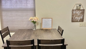 A dining area with a wooden table and four chairs, a framed welcome sign, a vase with flowers, and a wall-mounted sign saying "Wine a little laugh a lot". - 2 Bdr 1 Bath Mountain View House (Tucson)