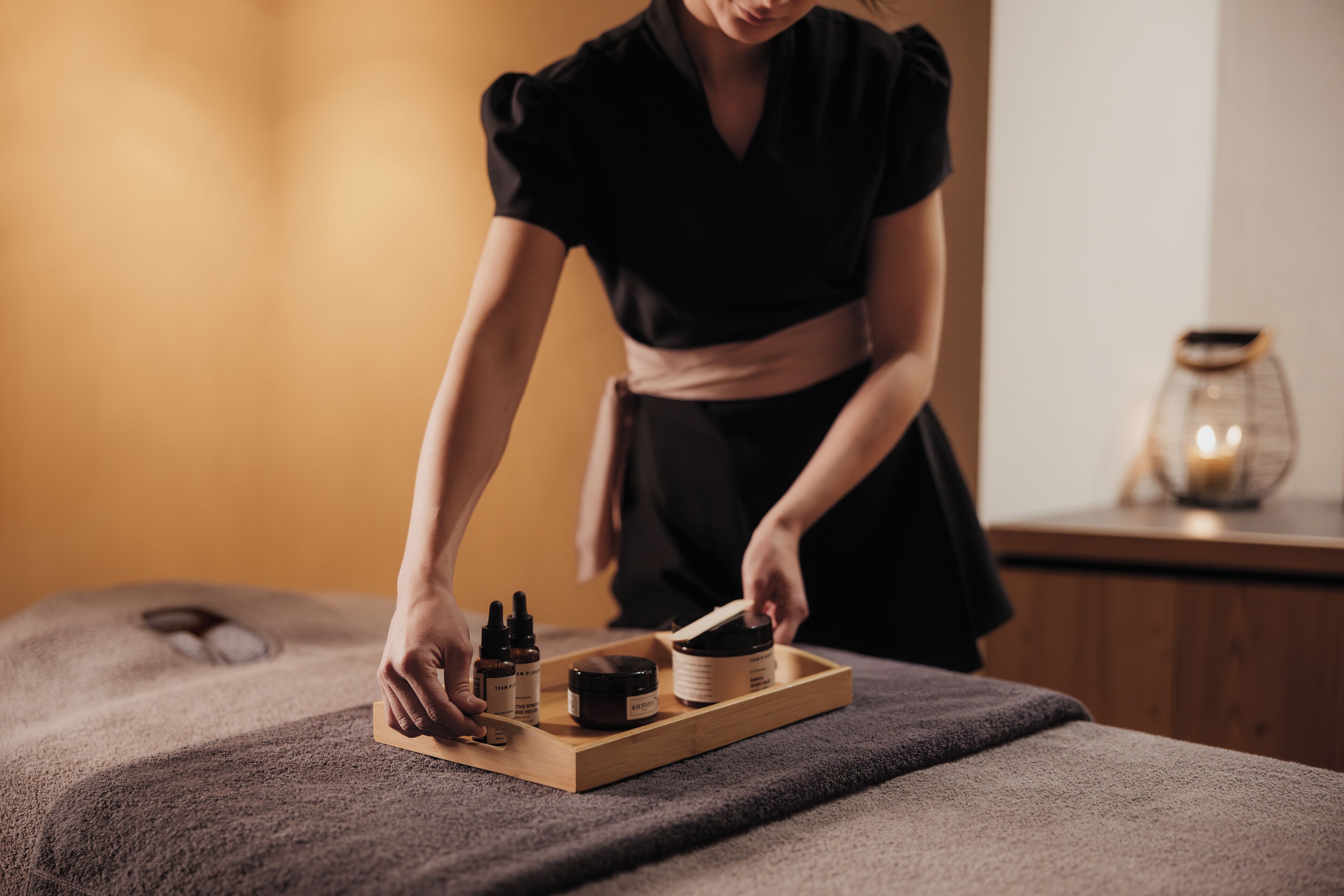Une personne dispose des produits de soins de la peau sur un plateau posé sur une table de massage.