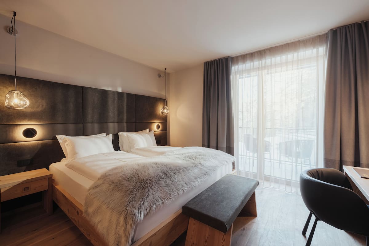 A modern hotel room with a large bed, wooden headboard, two bedside tables, a bench, a desk, and a chair.
