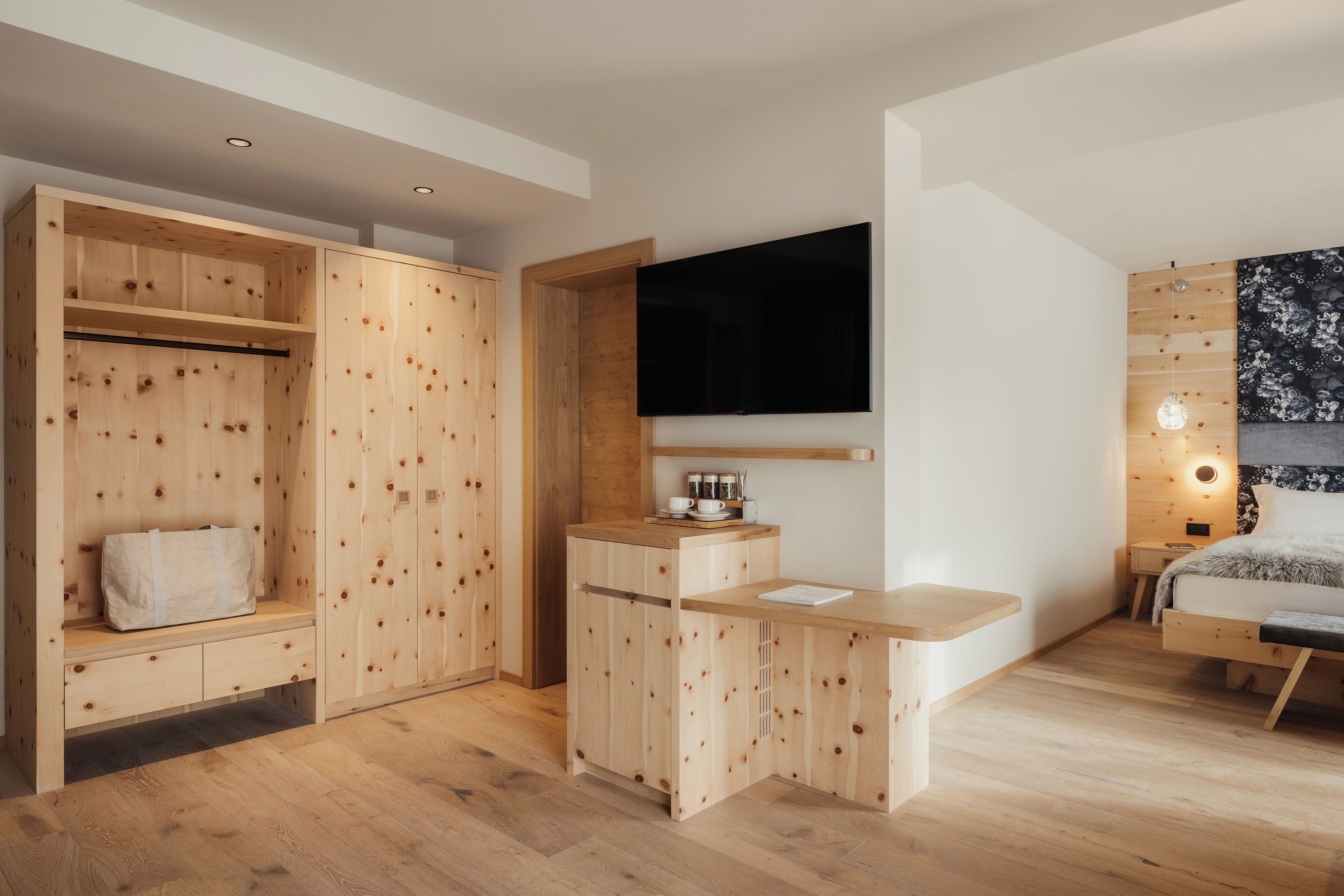 A modern bedroom with a wooden wardrobe, a flat-screen TV, a bedside table, and a bed with a patterned headboard.