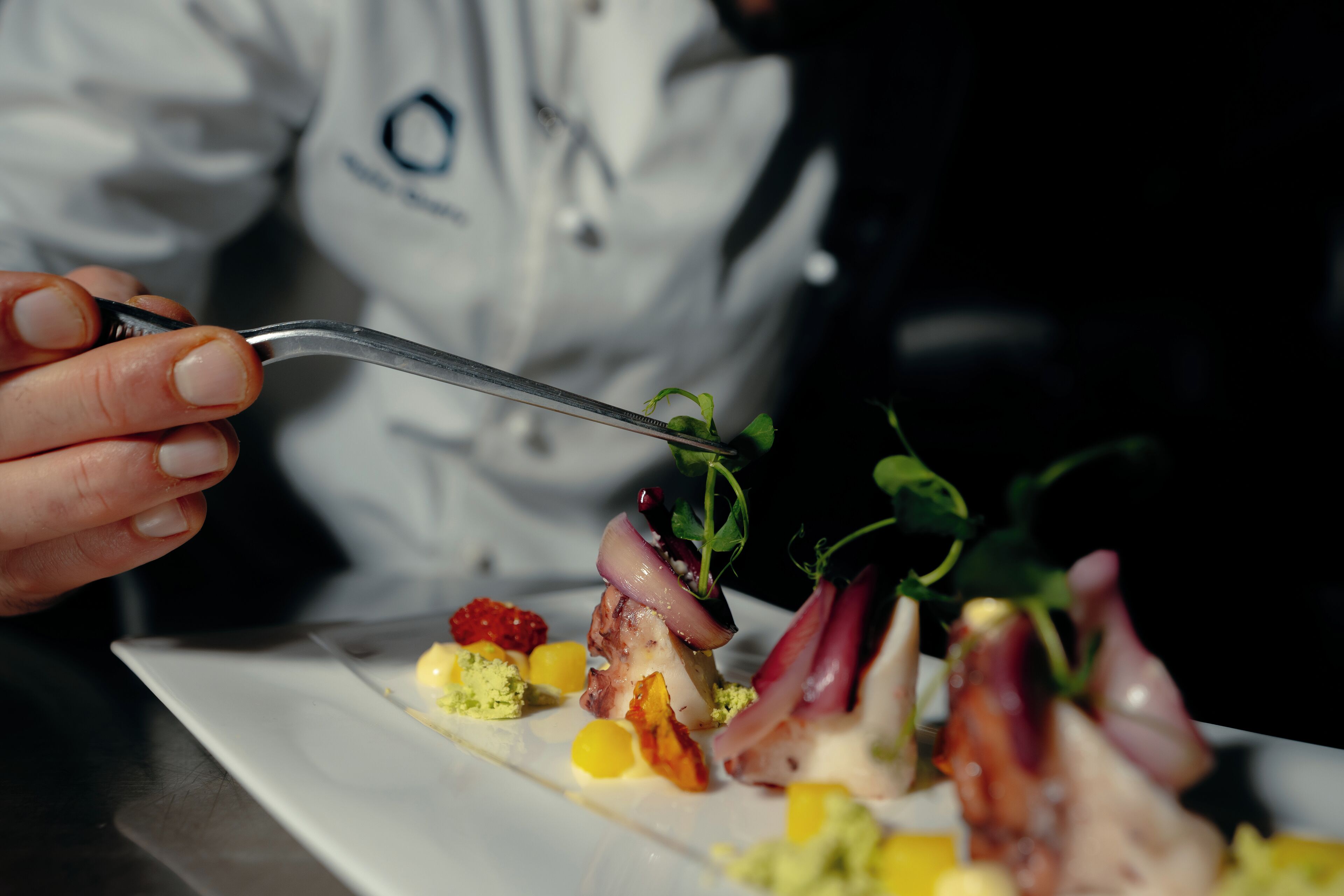 A chef holding a fork over a plated dish with various food items.