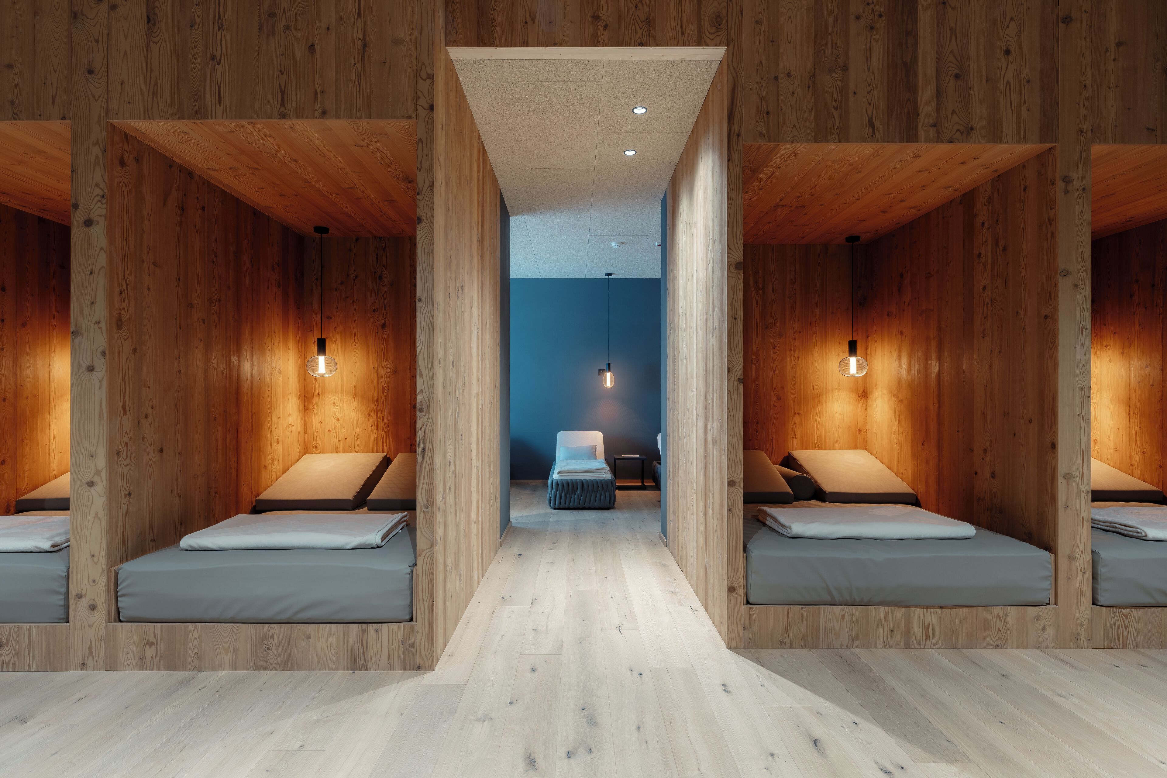 Ein Zimmer mit zwei Betten, Holzwänden, einer Sitzbank in der Mitte und Pendelleuchten.
