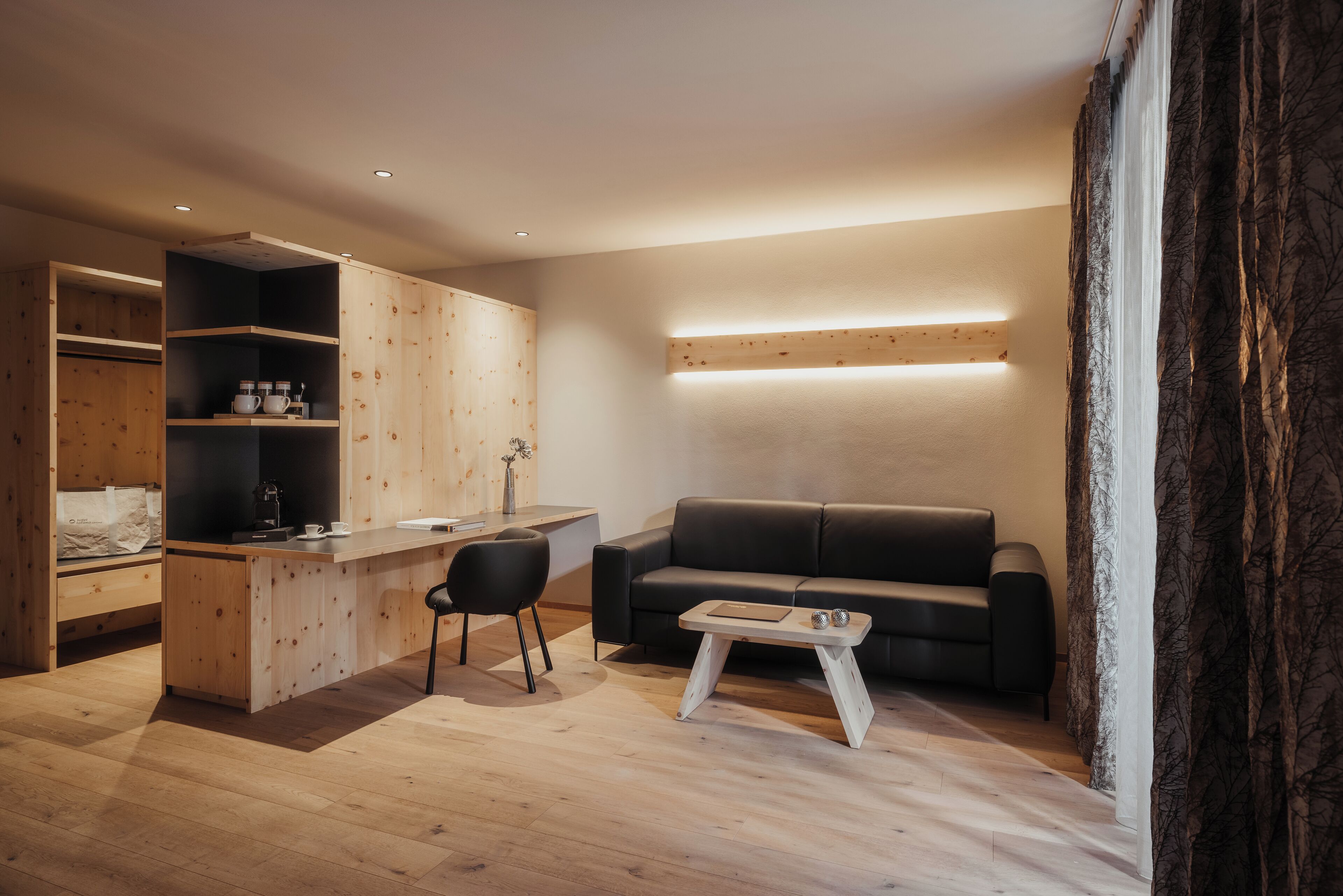 Un espacio habitable moderno con una kitchenette de madera, un sofá negro y una pequeña mesa de centro.