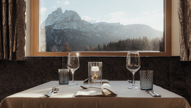 A table set for two with wine glasses, a candle, and a menu, overlooking a mountainous landscape.