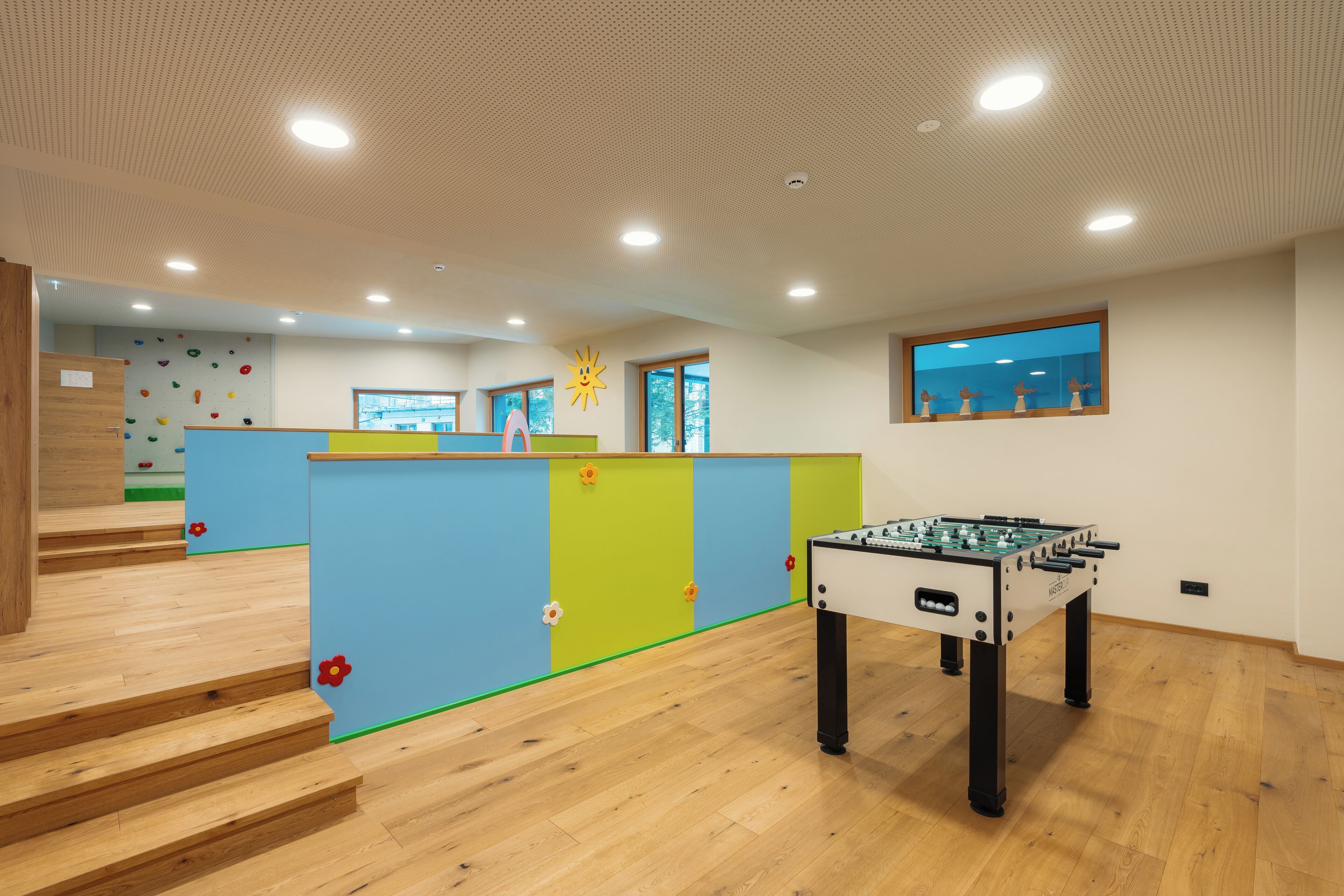 A modern indoor space with a foosball table, a climbing wall, and a staircase leading to another level.
