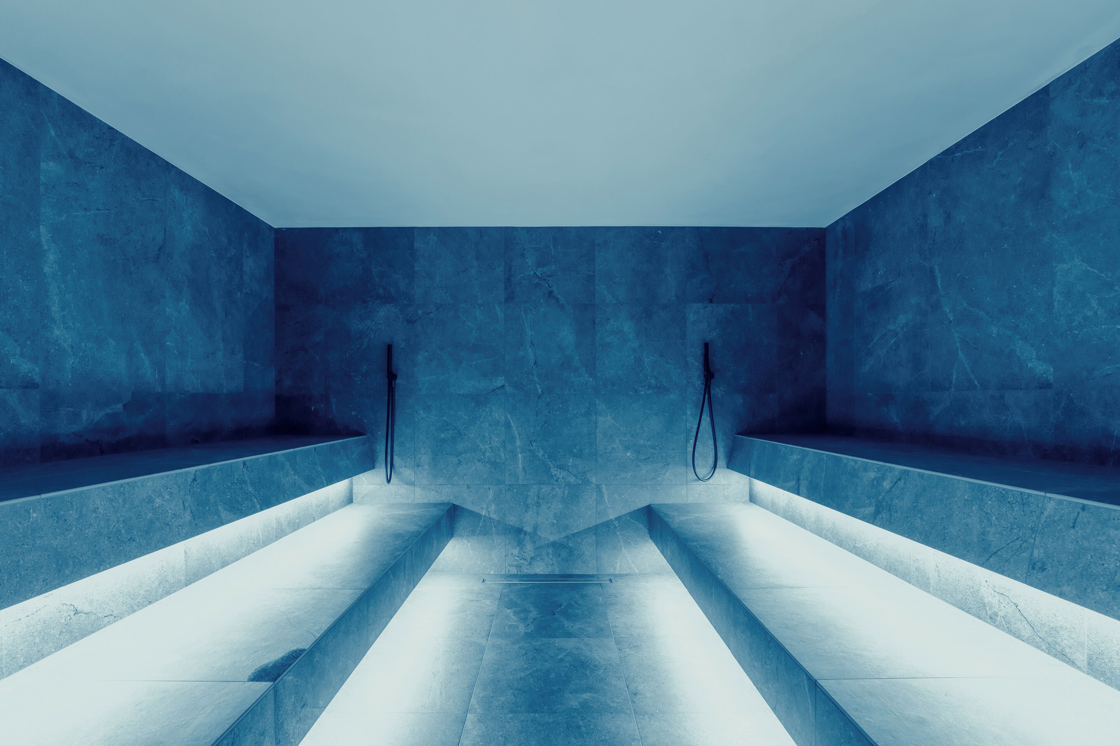 Ein modernes, minimalistisches Badezimmer mit blauen Marmorverkleidungen, einem zentralen Waschbecken und zwei Handtuchhaltern.