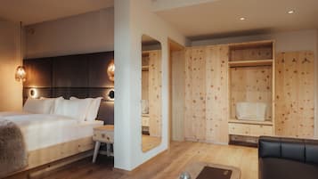 A modern hotel room with a large bed, a desk, a mirror, a seating area, and wooden storage units.