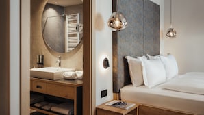 A modern hotel room with a large bed, a round mirror, a wooden vanity with a sink, and two pendant lights.