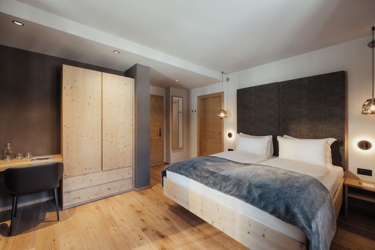 A modern bedroom with a large bed, wooden wardrobe, desk, and a pendant light.