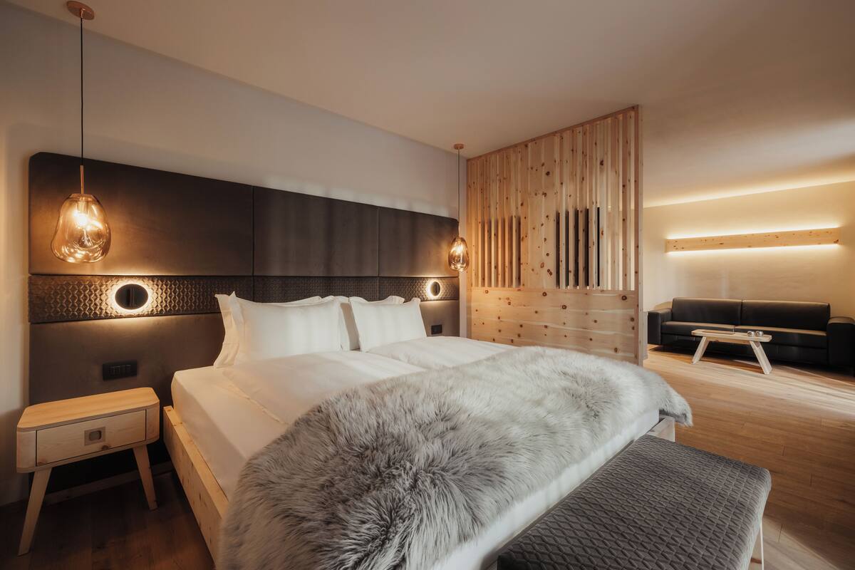A modern bedroom with a large bed, a wooden headboard, a nightstand, a dresser, and a seating area with a sofa and coffee table.