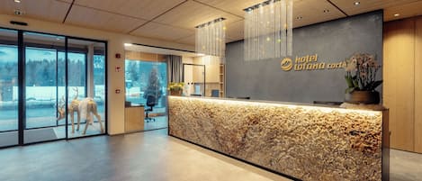 Ein Hotel-Empfangsbereich mit Marmor-Theke, Holzboden und Blick auf eine verschneite Landschaft durch die Glastüren.