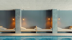 A modern indoor pool area with seating along the poolside, featuring light fixtures and a clear pool.