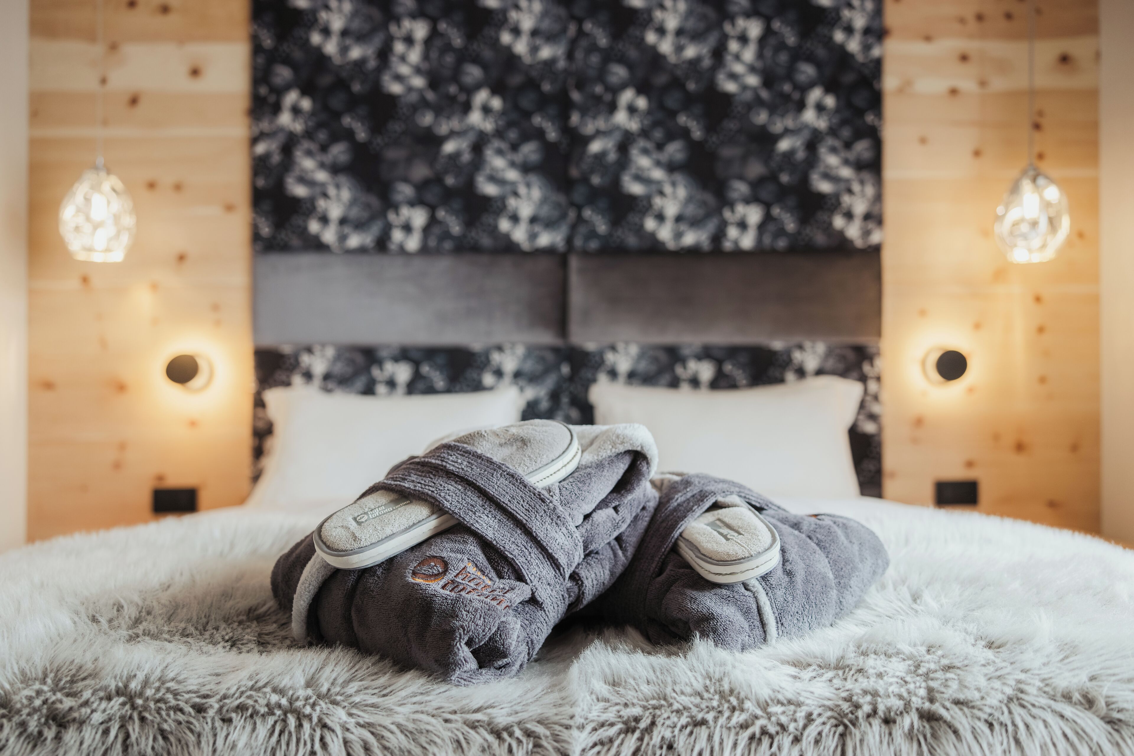 A bed with a fluffy white cover, two pillows, and a blanket rolled up at the foot of the bed.