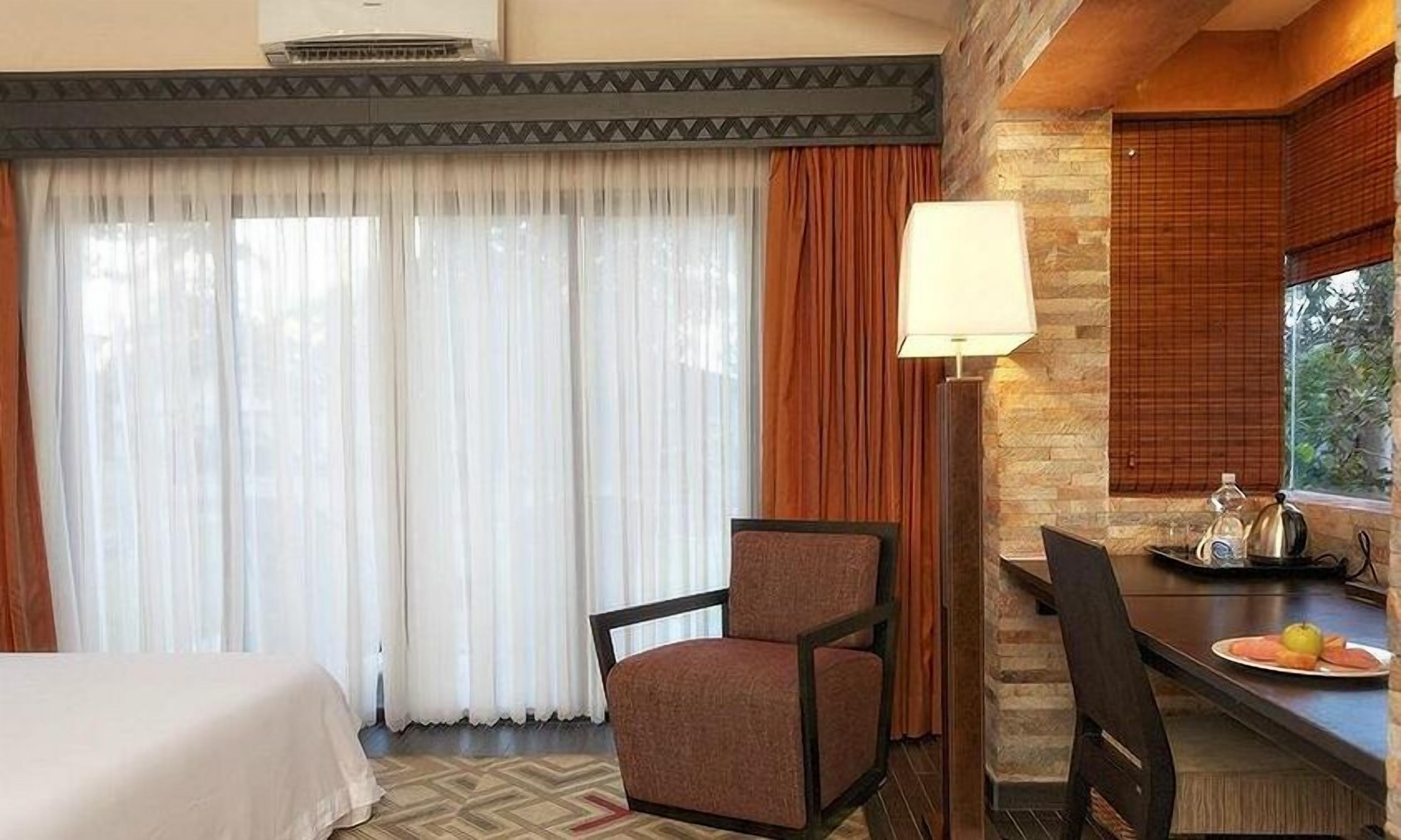 Una habitación de hotel con una cama, una silla, una mesa con un plato de comida y una lámpara.