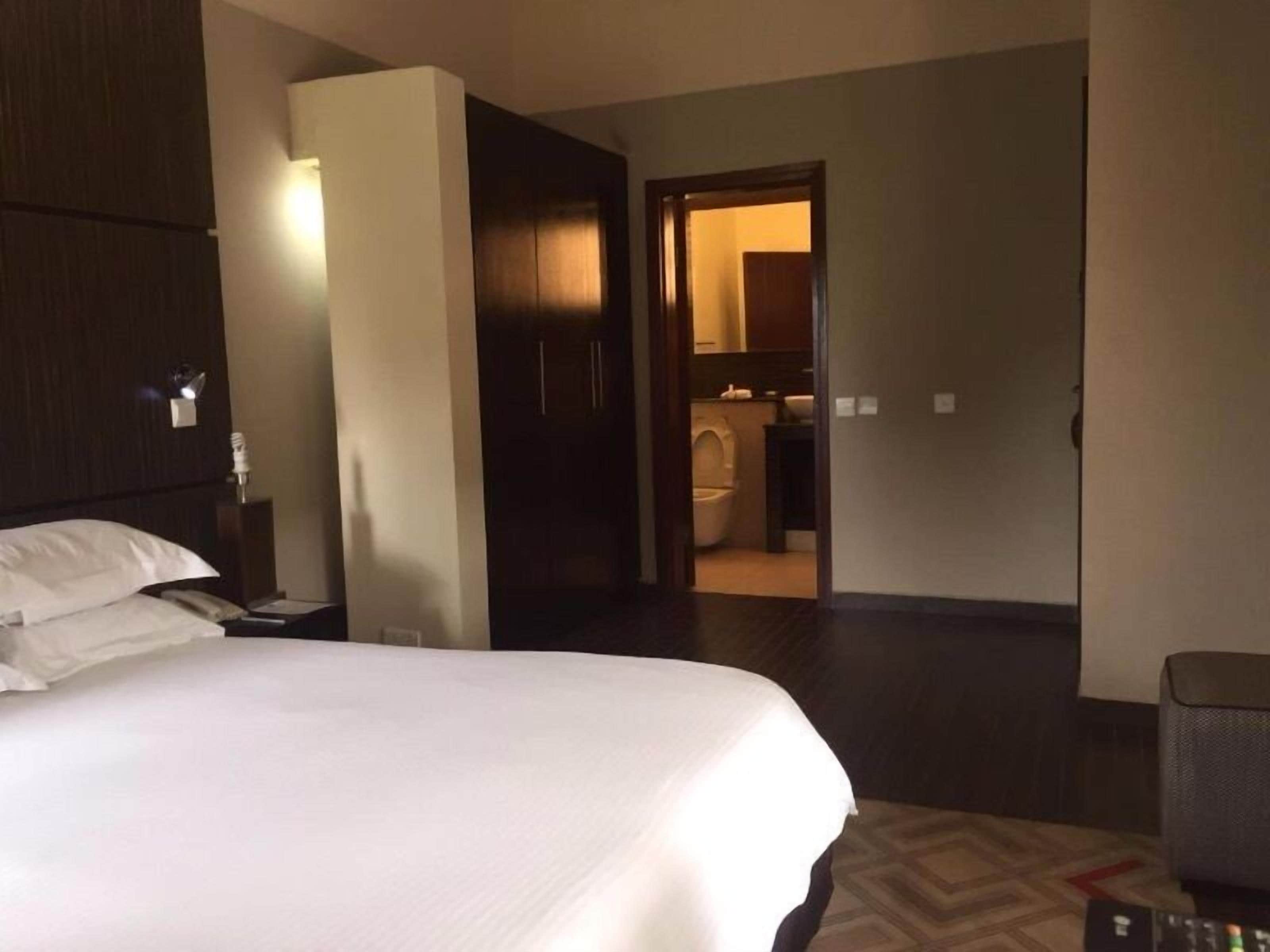A hotel room with a large bed, a nightstand, a lamp, and a door leading to a bathroom.