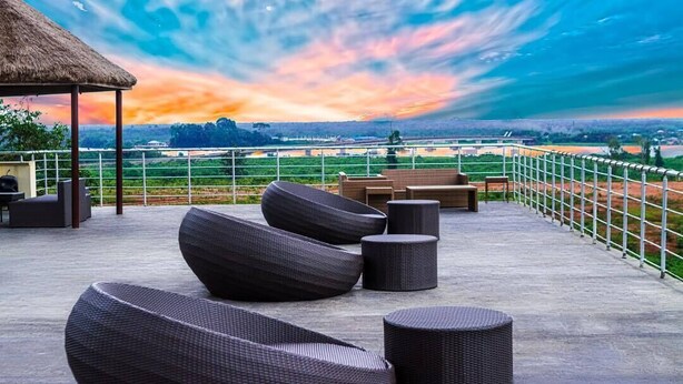 A rooftop terrace with outdoor seating, a thatched roof structure, and a scenic view of a landscape with a river and distant hills. - Epe Resort and SPA (Epe)