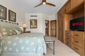 Un dormitorio con cama, televisor, armarios de madera y ventilador de techo.