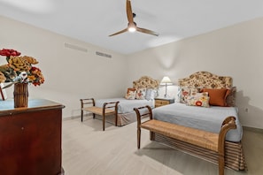 Un dormitorio con dos camas, un ventilador de techo, una mesita de noche con lámpara y un aparador de madera.