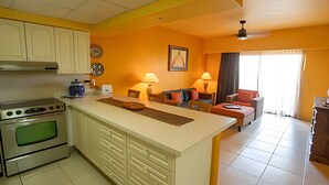 A compact kitchen with a central island, a dining area with a sofa, and a living room with a TV. - Condominio 1HAB/Balcón - Grand Marina Villas (Nuevo Vallarta)