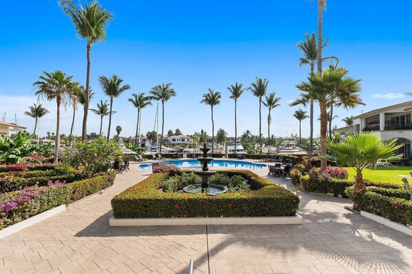 A pool area with palm trees, a fountain, and a well-maintained garden. - Condominio 1HAB/Balcón - Grand Marina Villas (Nuevo Vallarta)