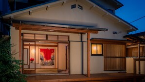 A traditional Japanese house with a wooden exterior, a sliding door entrance, and a small garden area visible through the doorway.