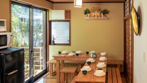 A traditional Japanese-style room with a wooden table set for tea, a microwave, and a sliding glass door to a garden.
