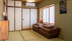 A traditional Japanese room with tatami flooring, a futon bed, sliding doors, and a fan.