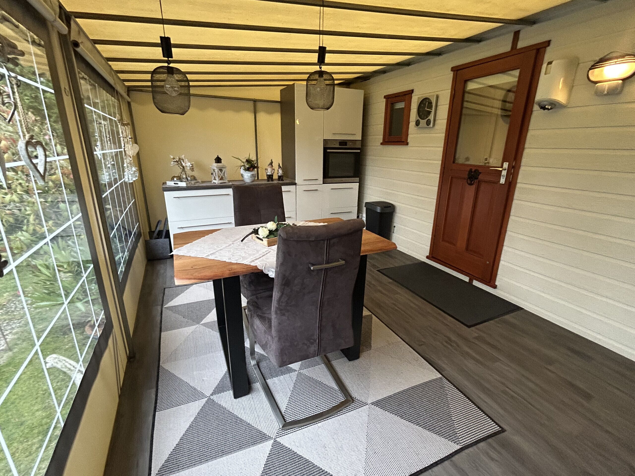 A compact kitchen with white cabinets, a wooden table, and a patterned rug.
