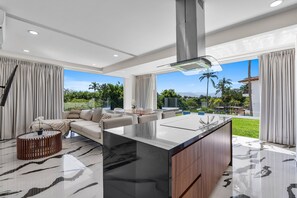 A modern kitchen with a central island, large windows, and a view of a tropical landscape. - 2BR Residence • Private Pool • Canal • Beach (Las Jarretaderas)