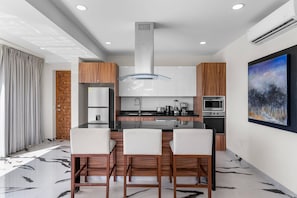 A modern kitchen with a central island, bar stools, and a painting on the wall.