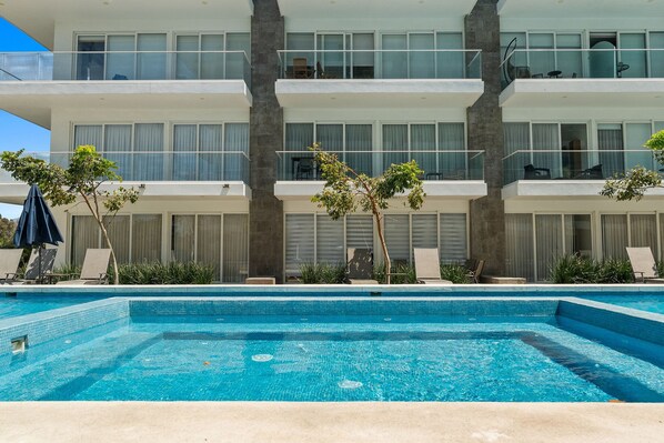 A multi-story hotel with a swimming pool, outdoor seating, and a view of the surrounding area.