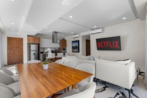 A modern living space with a dining area, kitchen, and a large wall-mounted television. - 2BR Residence • Private Pool • Canal • Beach (Las Jarretaderas)