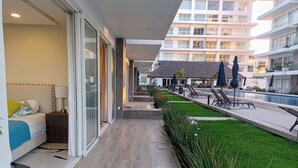 A hotel room with a bed, a nightstand, and a view of a pool area with lounge chairs and umbrellas. - 2BR Exclusive Private Pool • Canal view y Beach (Las Jarretaderas)