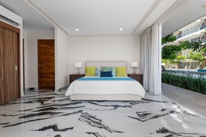 A modern hotel room with a large bed, two bedside lamps, a wooden door, and a view of a swimming pool and greenery. - 2BR Residence • Private Pool • Canal • Beach (Las Jarretaderas)