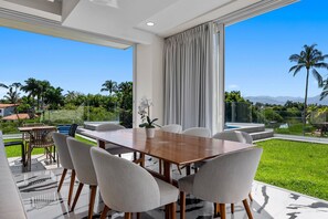 A modern dining area with a large table and chairs, a potted orchid, and a view of a lush garden and mountains. - 2BR Residence • Private Pool • Canal • Beach (Las Jarretaderas)